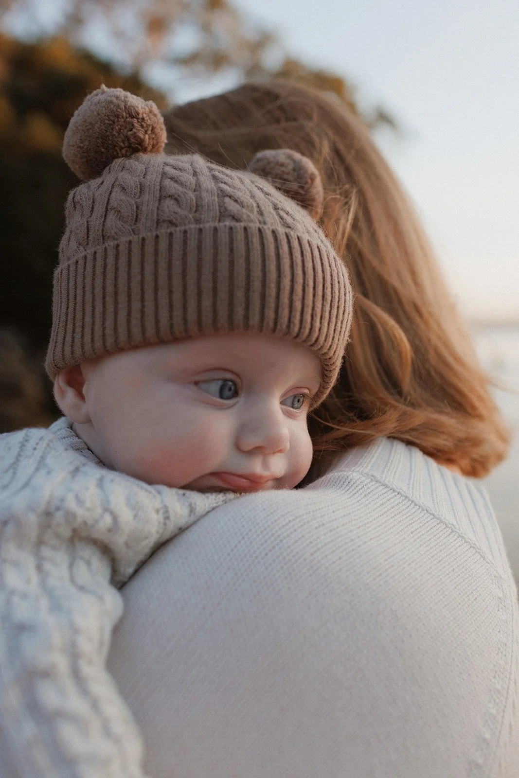 Mother cuddling baby wearing teddy bear hat