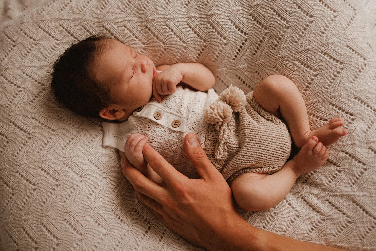 Newborn baby asleep on knit blanket, holding father's hand