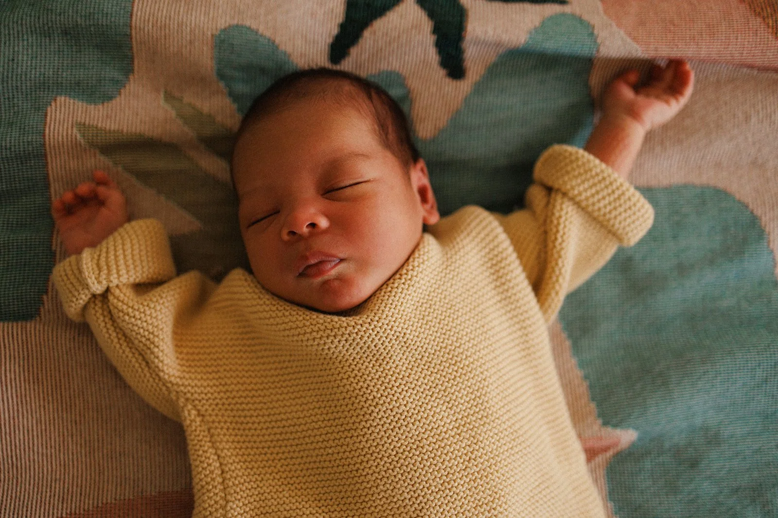 Newborn baby in yellow jumper lying on bed
