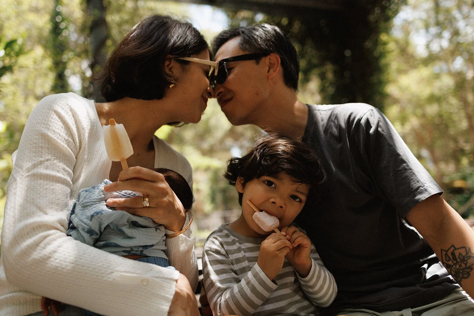 Family with newborn baby and toddler eating ice creams in park together
