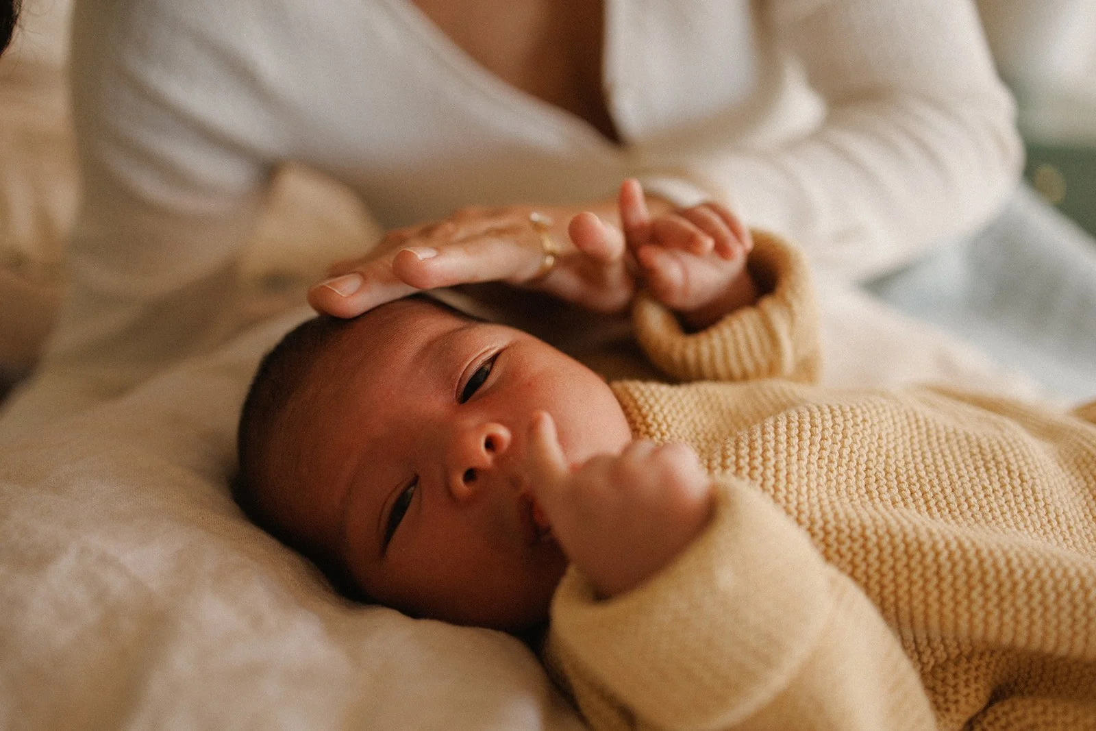 Newborn baby lying on bed with mother stroking his head
