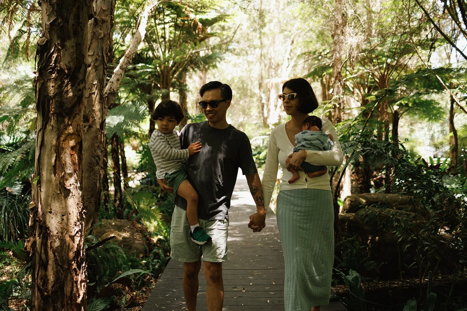 Couple holding hands and carrying newborn baby and toddler walking in the park