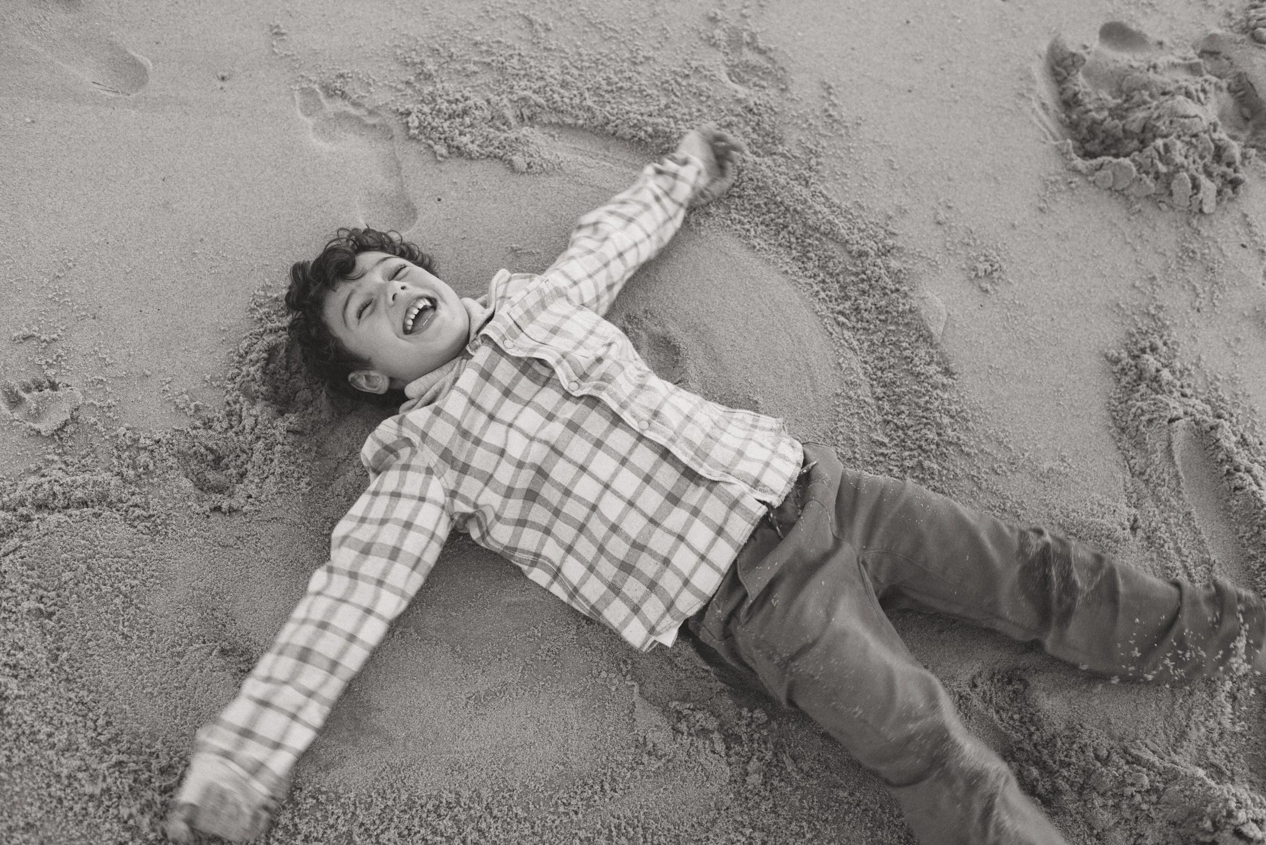 Young boy making snow man shape in the sand on the beach