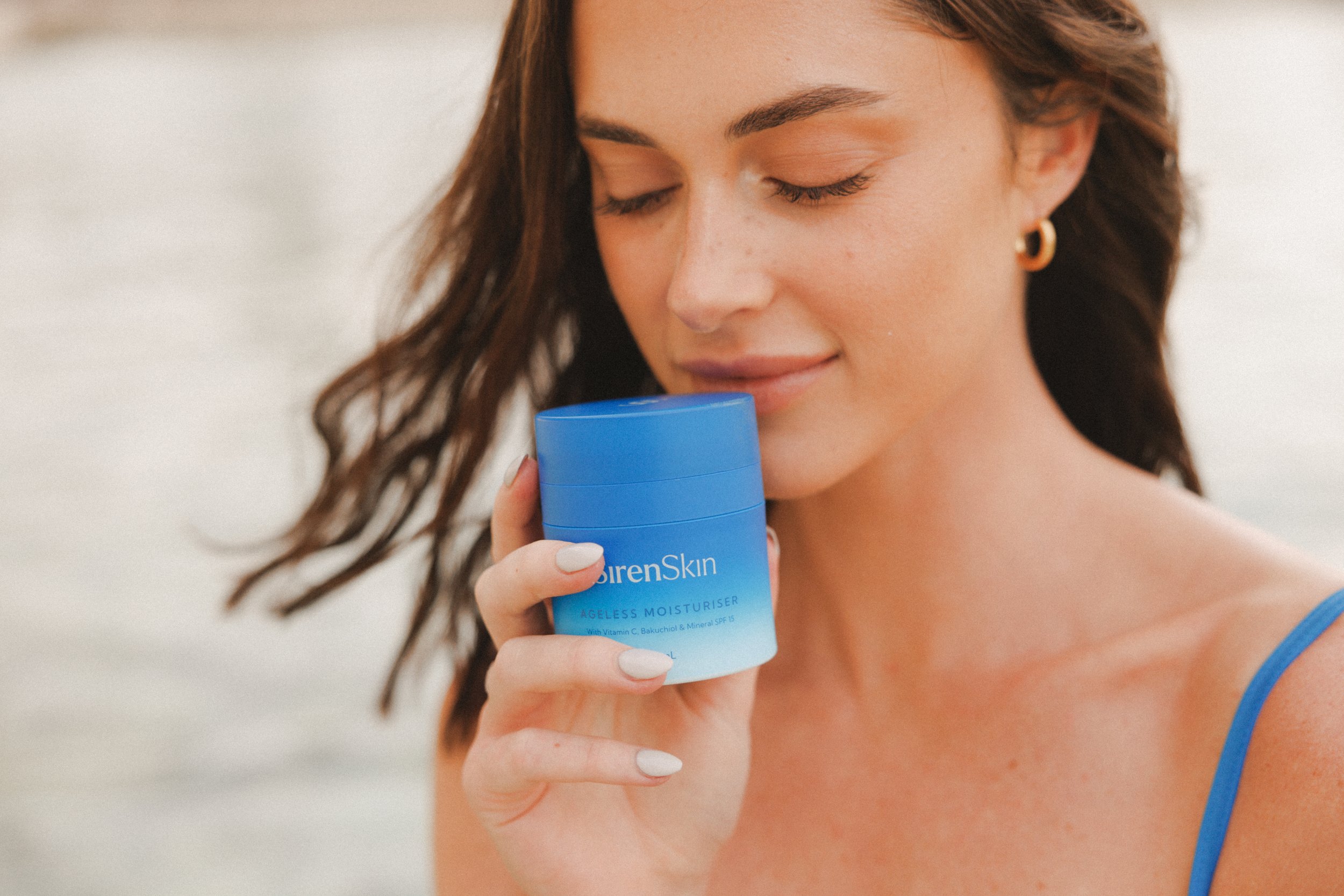 Woman holding Siren Skin moisturiser at the beach