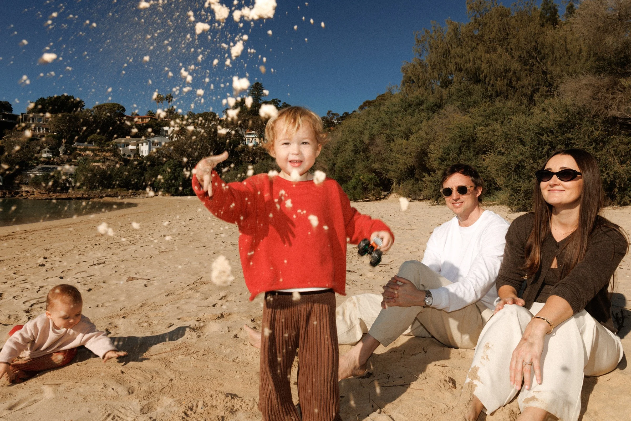 Child throwing sand into the air while the family plays on the beach.