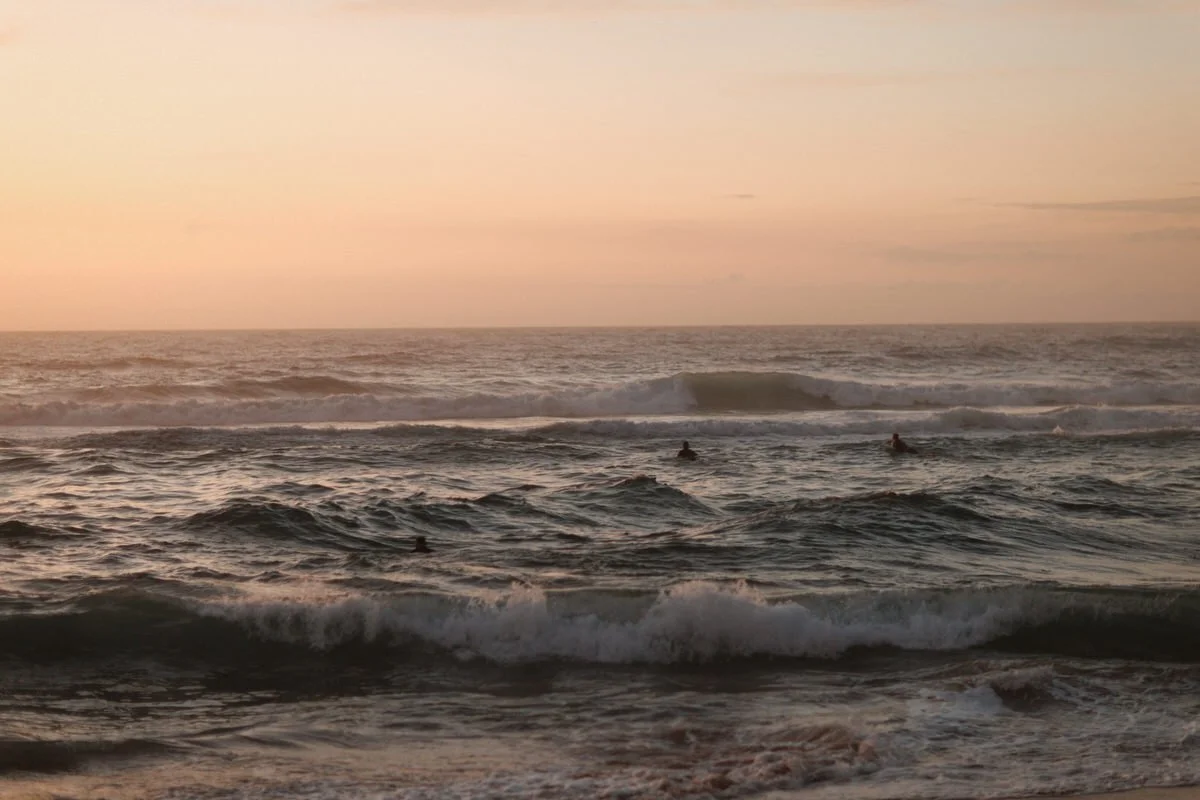 Beach scene during sunset with ocean waves and surfers in the water.