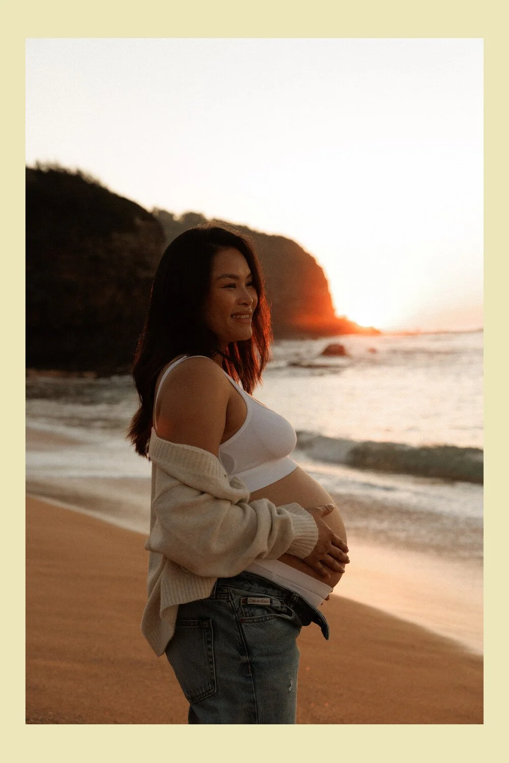 Pregnant mother cradling her baby bump beside the ocean in Sydney winter morning light.