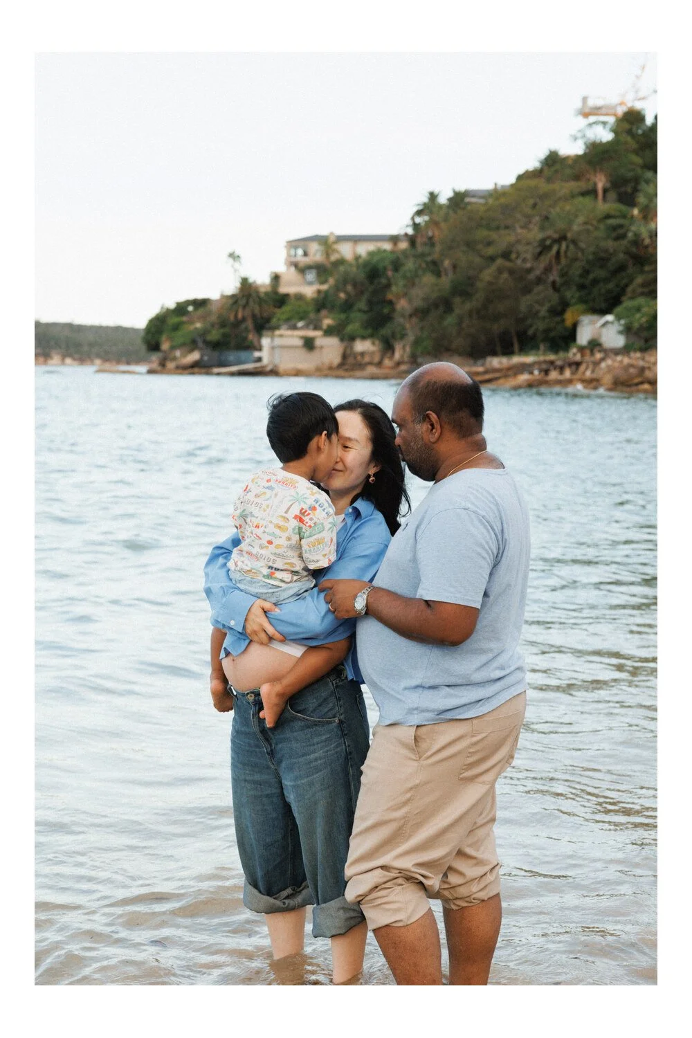 Family embrace: Parents cuddling their toddler while standing in shallow water.