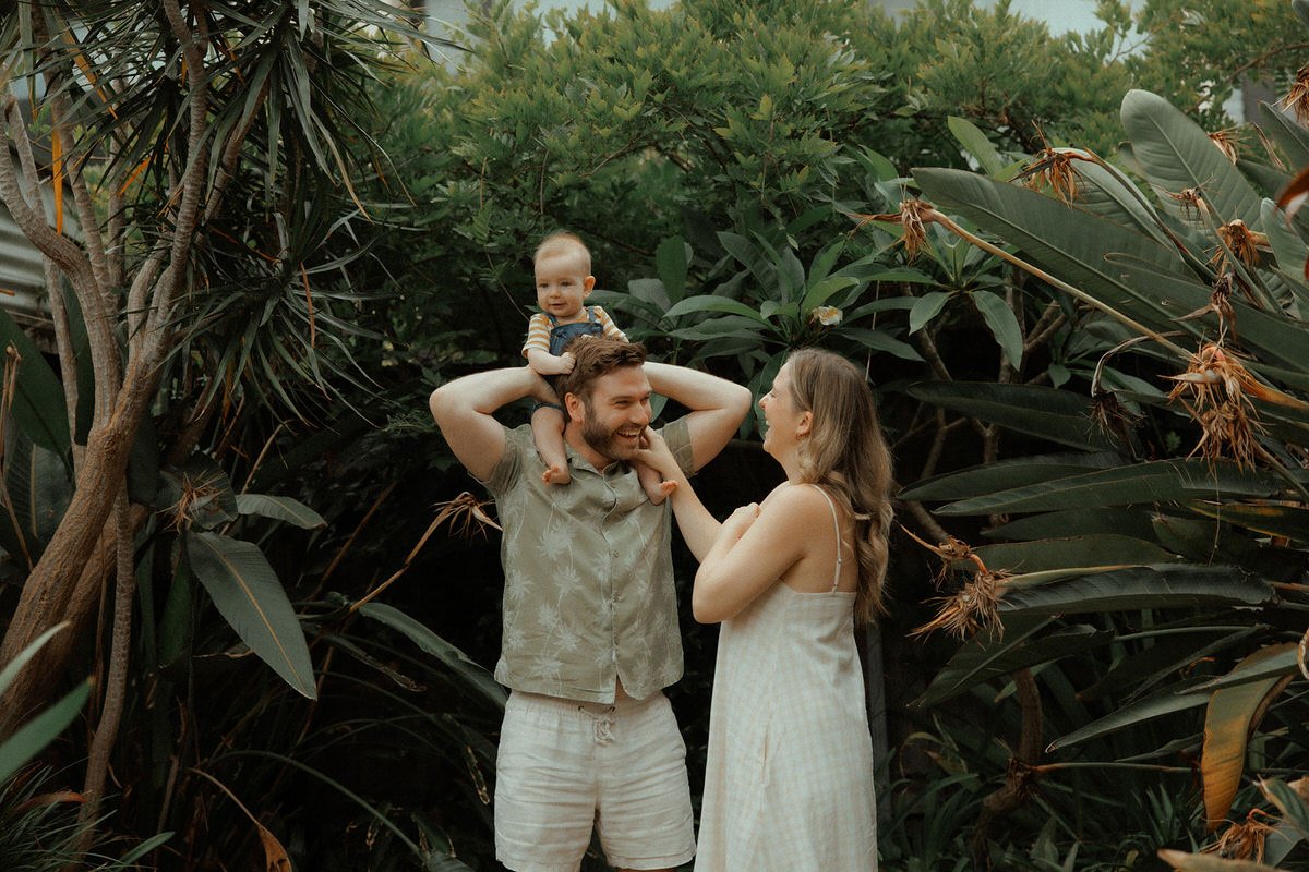 A family, including a man, woman, and a baby, standing among lush green tropical plants, sharing a joyful moment together.