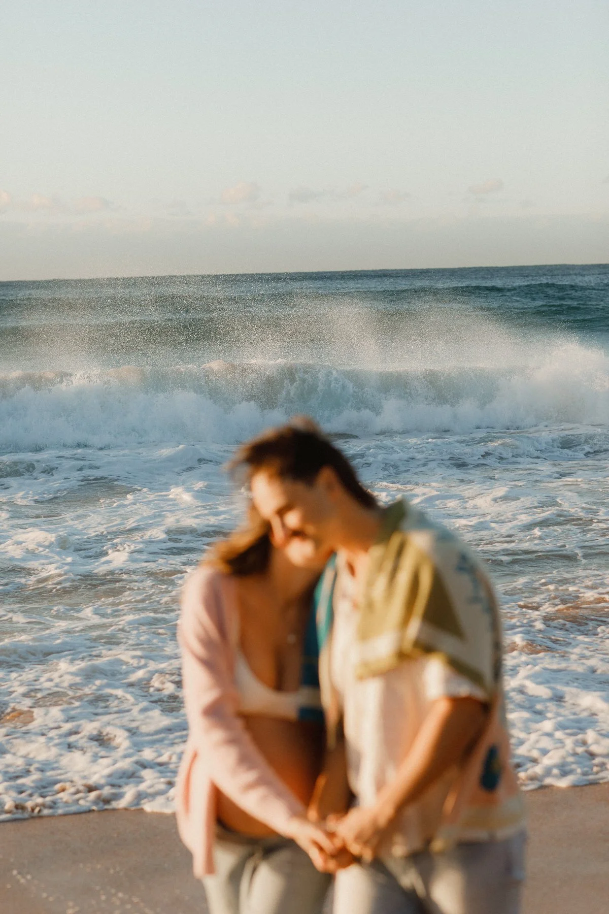 Blurred woman in a pink jacket smiling at the beach, with ocean waves and the sky in the background.