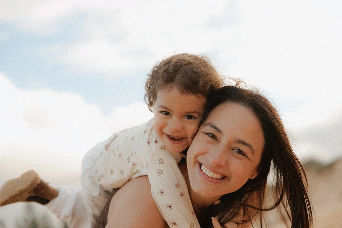 A young woman and a small child smiling and playing outdoors on a cloudy day.