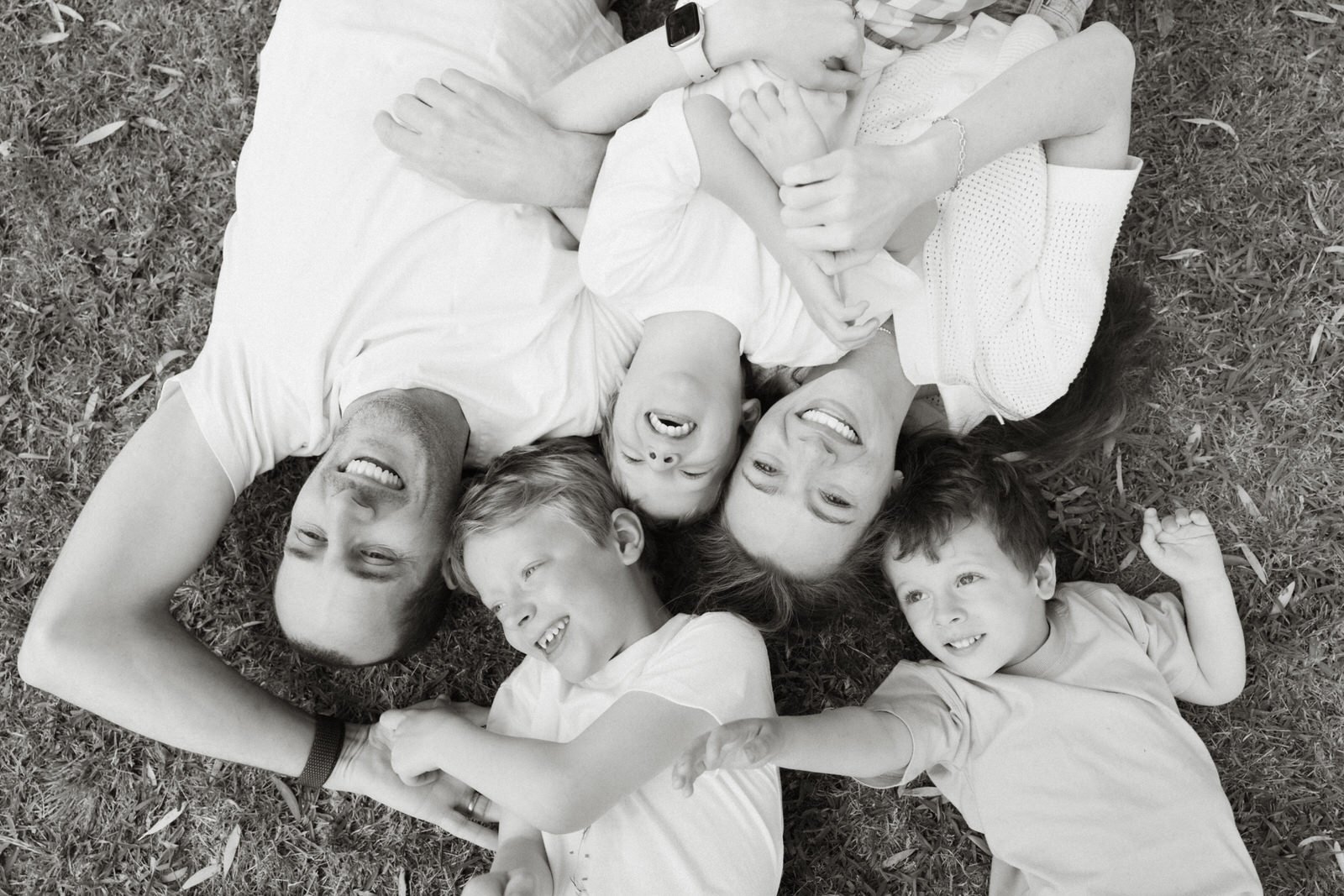A family of six lying on the grass, smiling and laughing, with their heads close together.