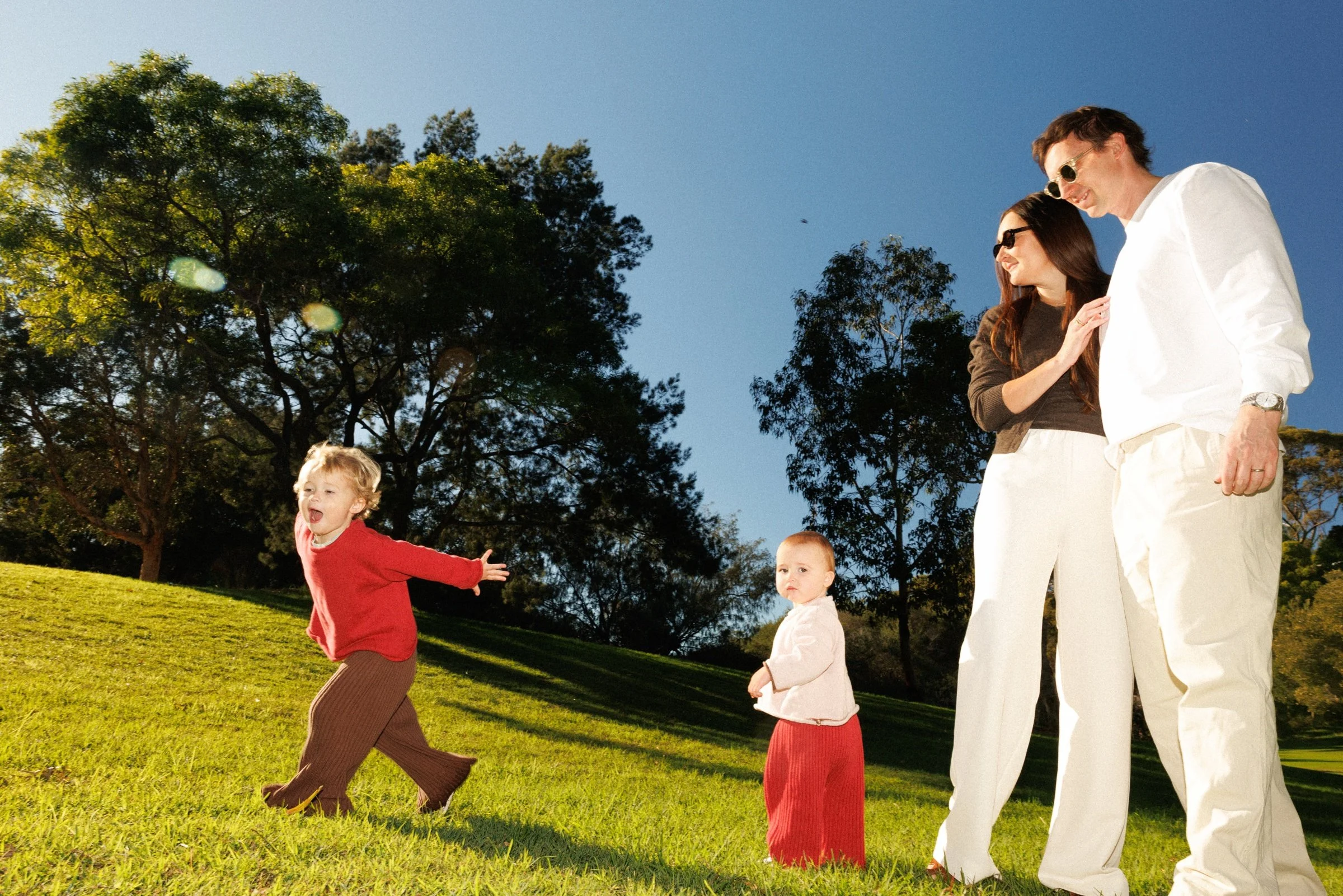 Family playing on bright green grass, with red clothing standing out against the blue sky.