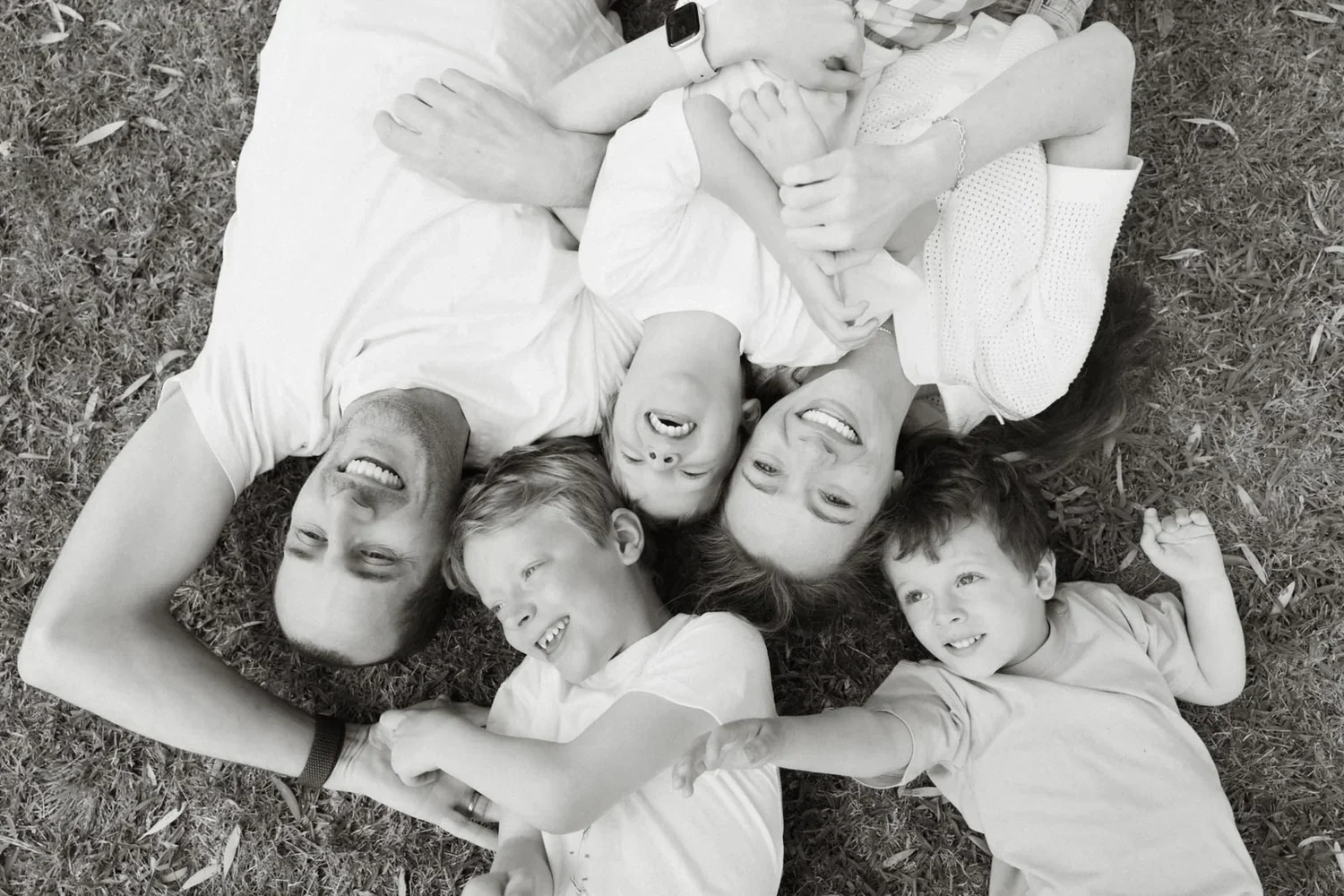 A family laughing together, lying head to head on the grass in black and white.