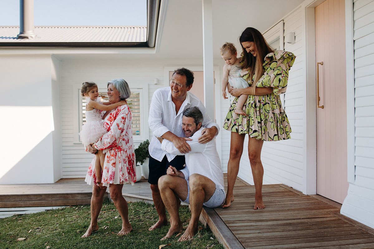 A multigenerational family laughing and playing on a balcony outside a house.