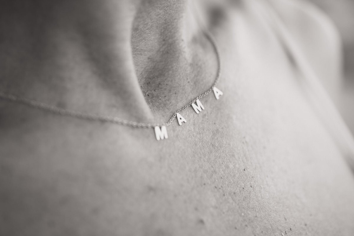 Close-up of a woman's neck and collarbone wearing a necklace with the word 'MAMA' spelled out in silver letters.
