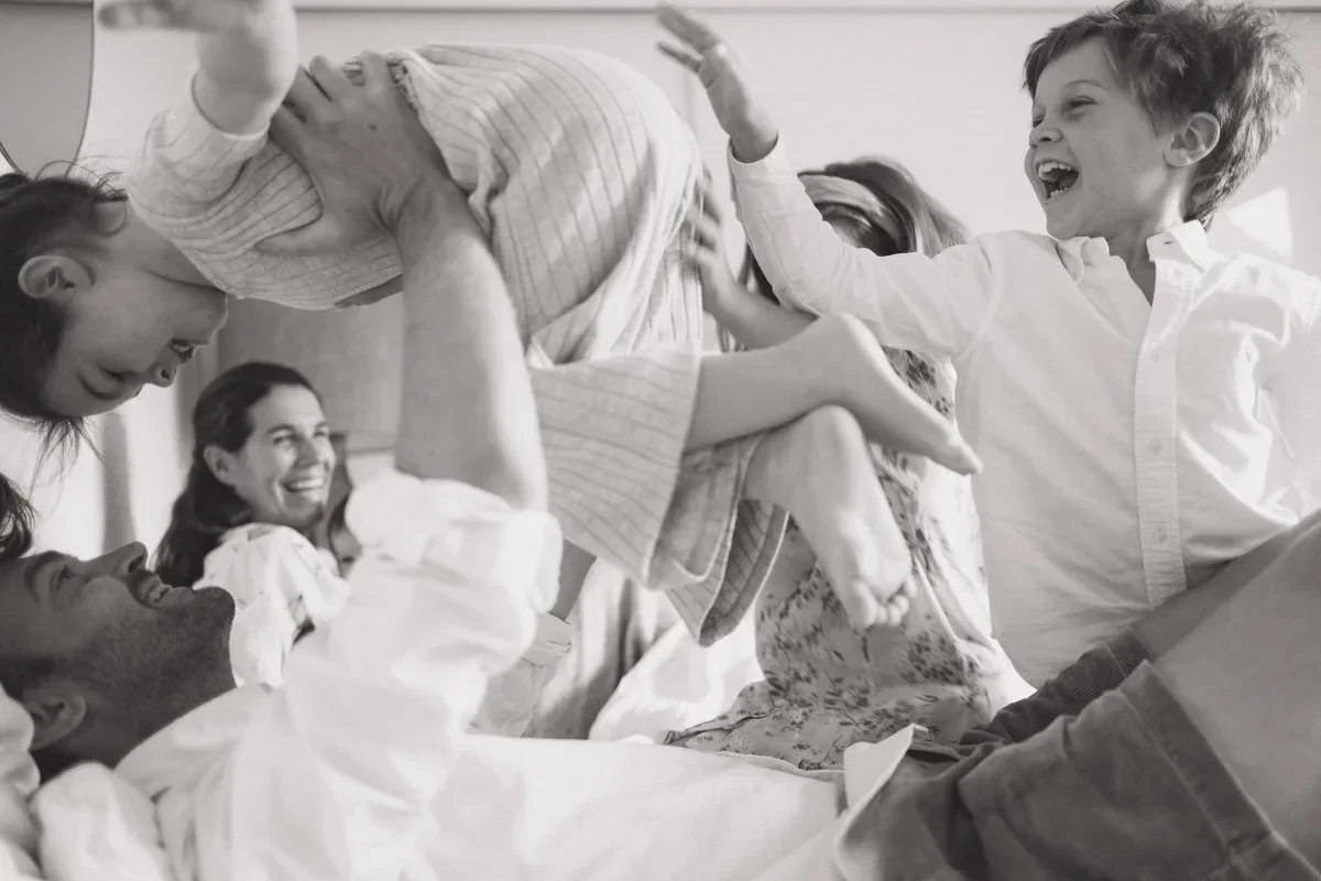 A family laughing and tumbling together on a bed in black and white.