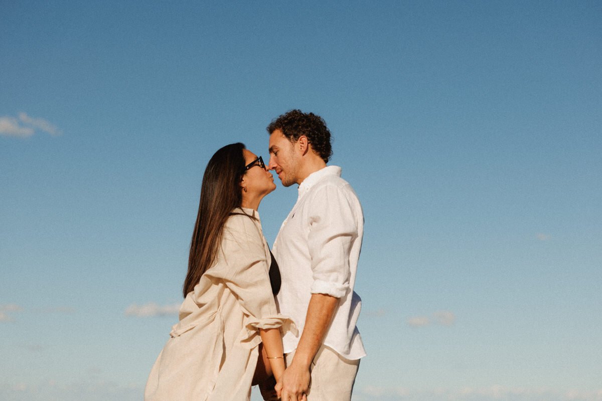 A couple standing close together outdoors, about to kiss, with a blue sky in the background.