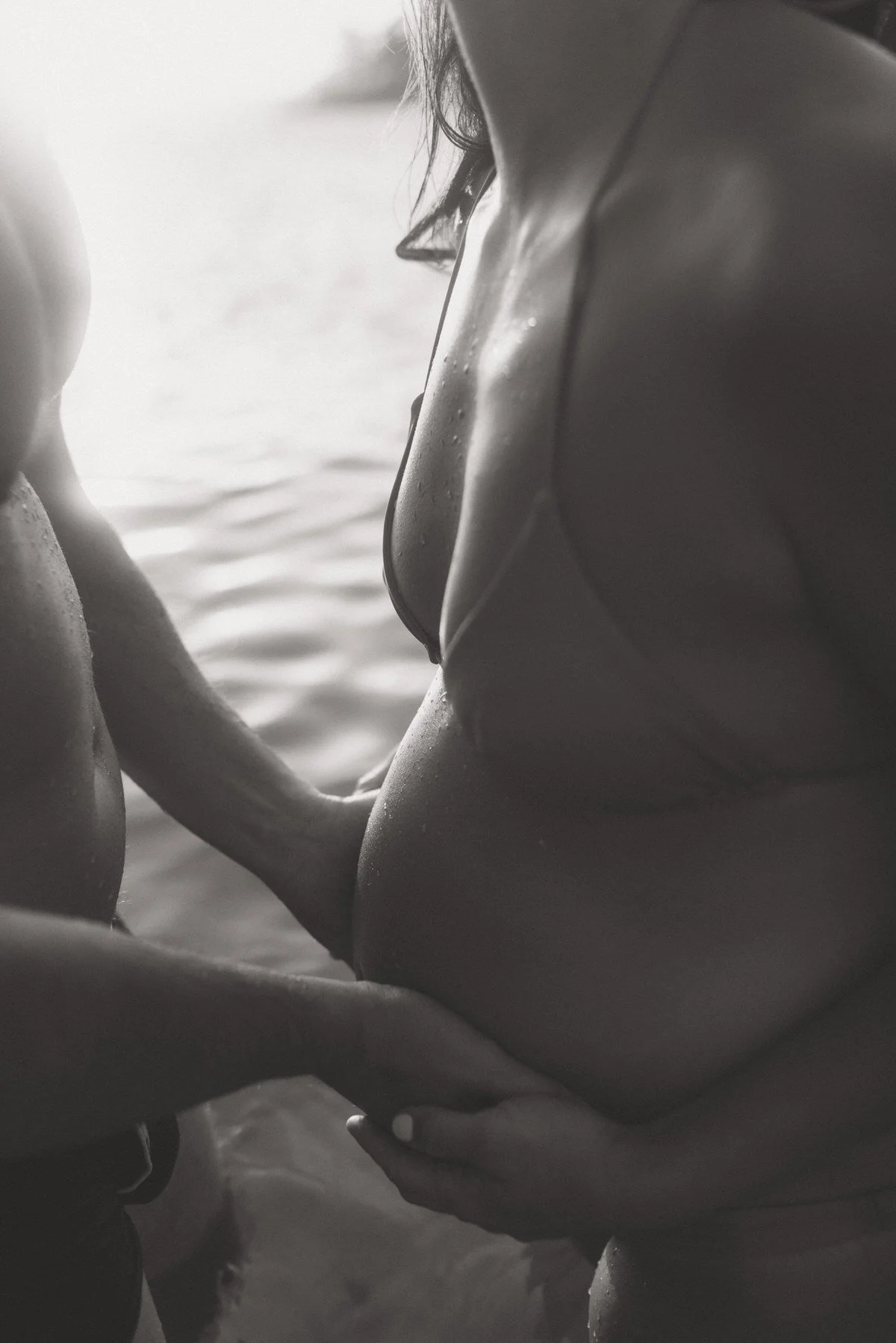 Black and white photo of a woman touching her chest, wearing a bikini.