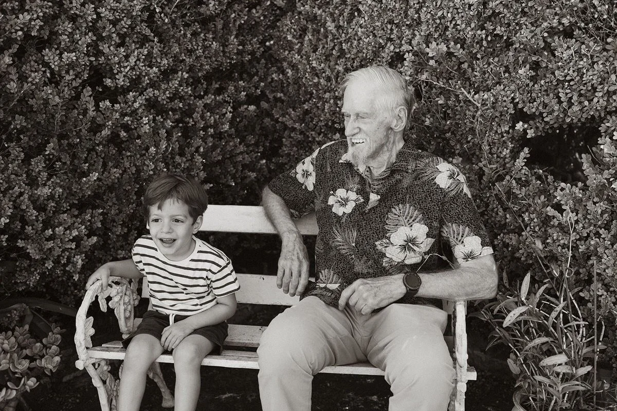 A grandfather and child laughing on a garden bench in black and white.