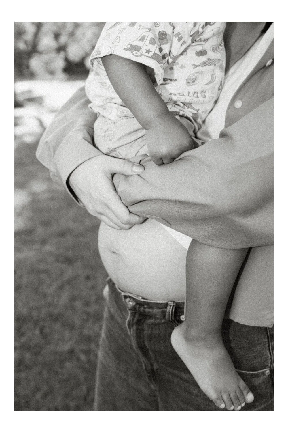 Little details: Black and white close-up of a mother’s bump, hands and her toddler’s bare feet.