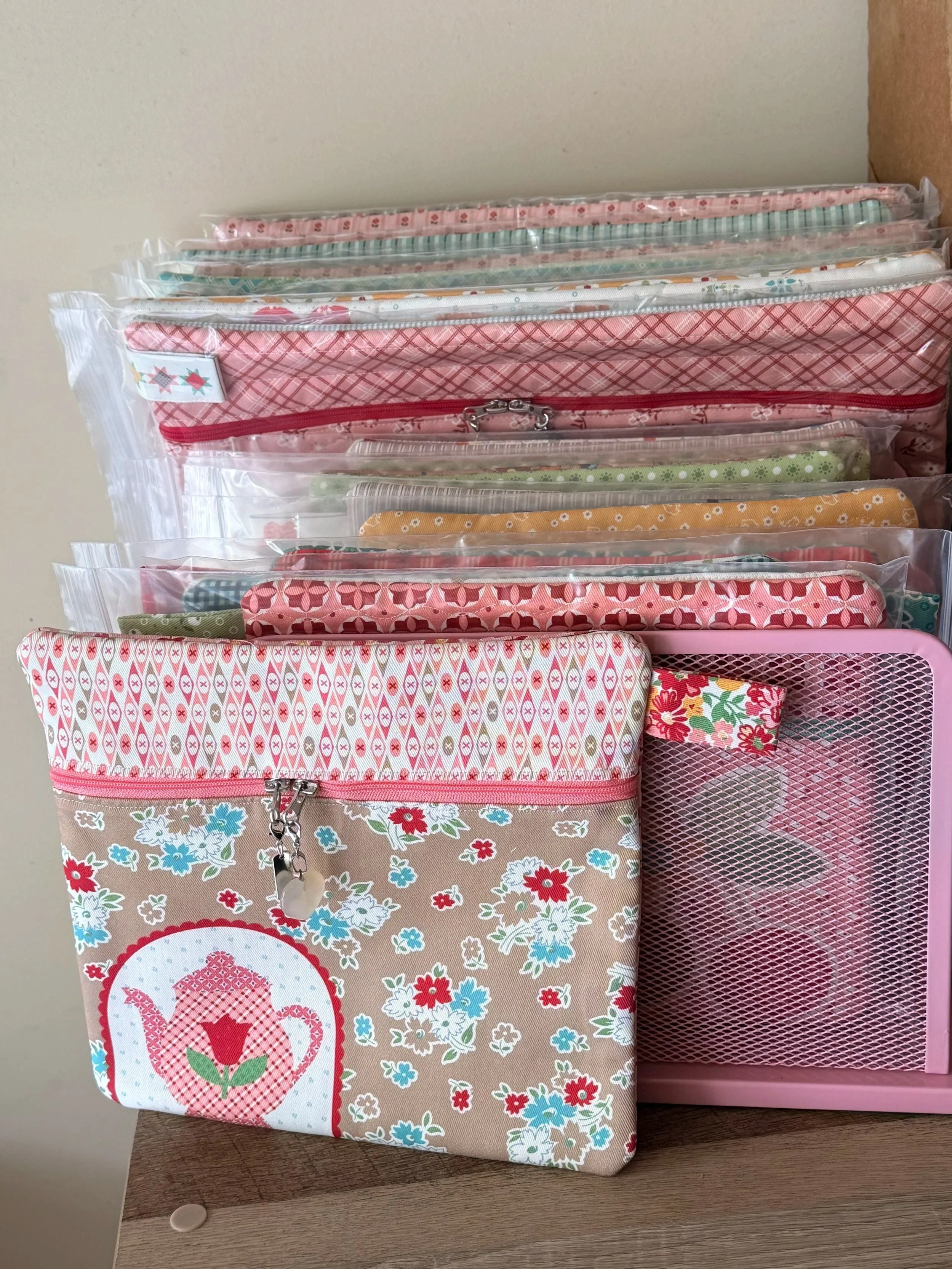 A pink and floral printed fabric pouch with a keychain and zipper, placed on top of a wooden surface and next to a pink mesh storage organizer with floral fabric inside.