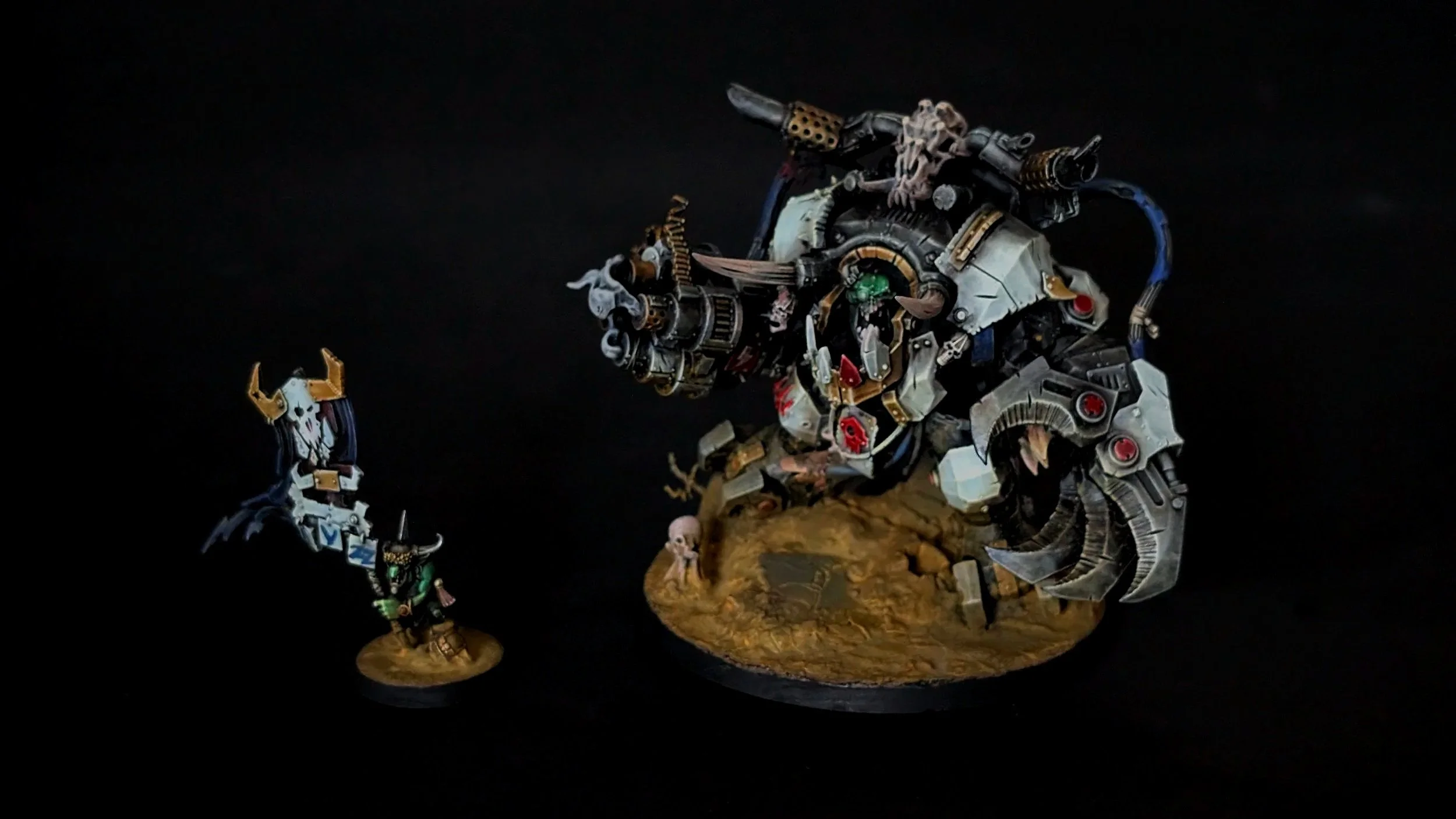 Figurines de soldats et mécanismes inspirés de fantasy ou de science-fiction, représentant une scène de combat ou de confrontation dans un décor rocheux, avec un fond noir.