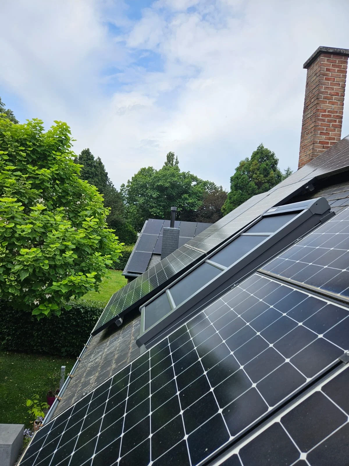 Toit avec panneaux solaires sur une maison entourée d'arbres verts et d'un ciel partiellement nuageux.