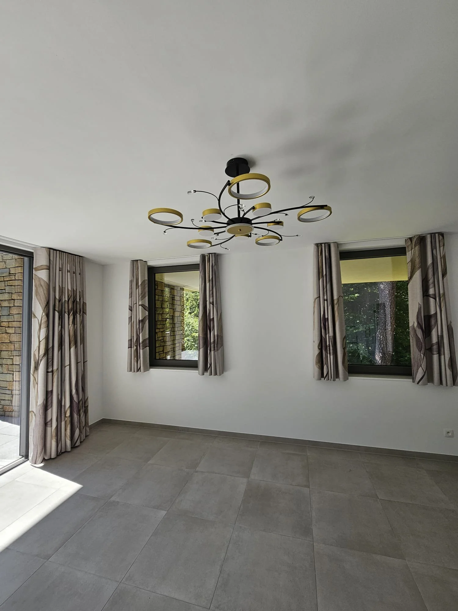 Salle de séjour avec de grandes fenêtres, rideaux à motifs, un plafond blanc et un luminiaire moderne.