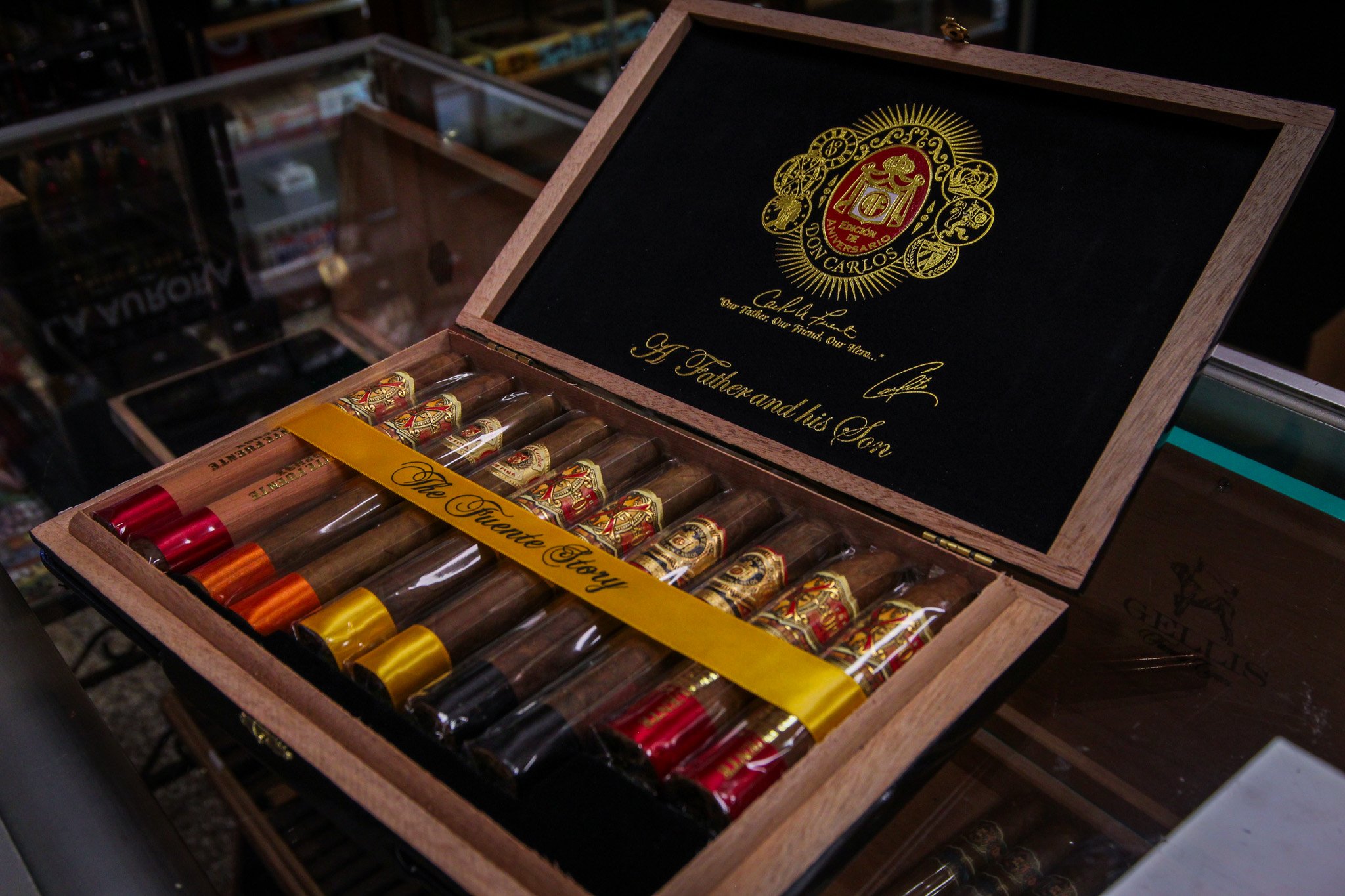Open wooden box of cigars with gold and red labels, inside a glass display case in a store.
