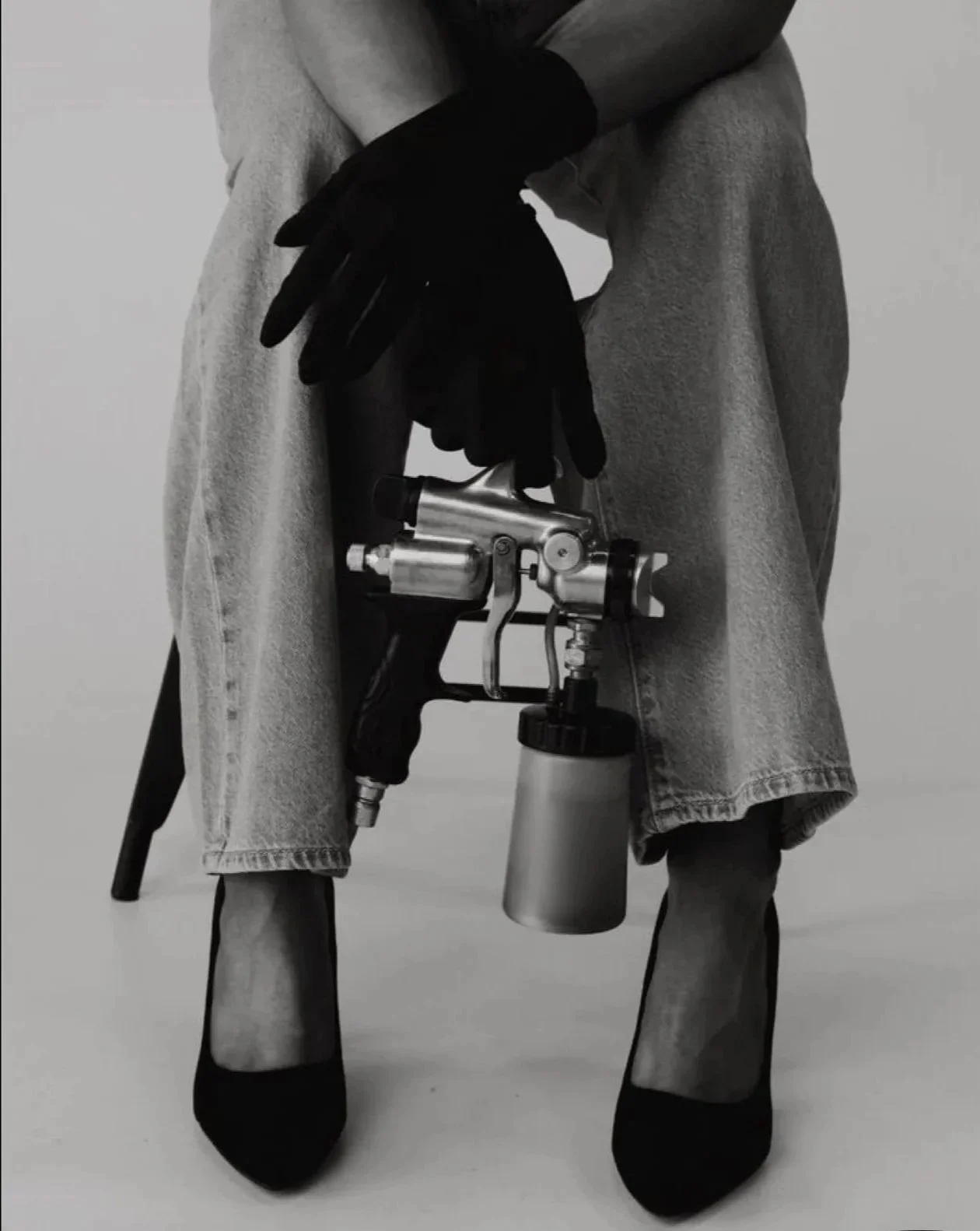 A woman wearing black gloves is holding a spray gun, preparing to paint or apply a coating.