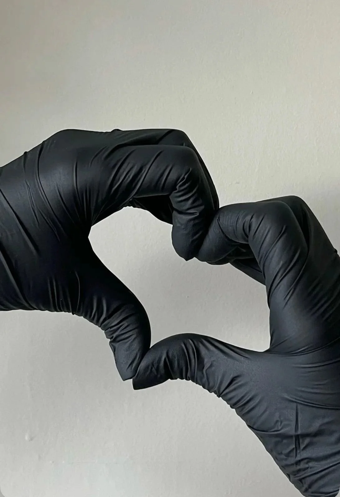 A pair of hands wearing black gloves forming a heart shape against a neutral background.