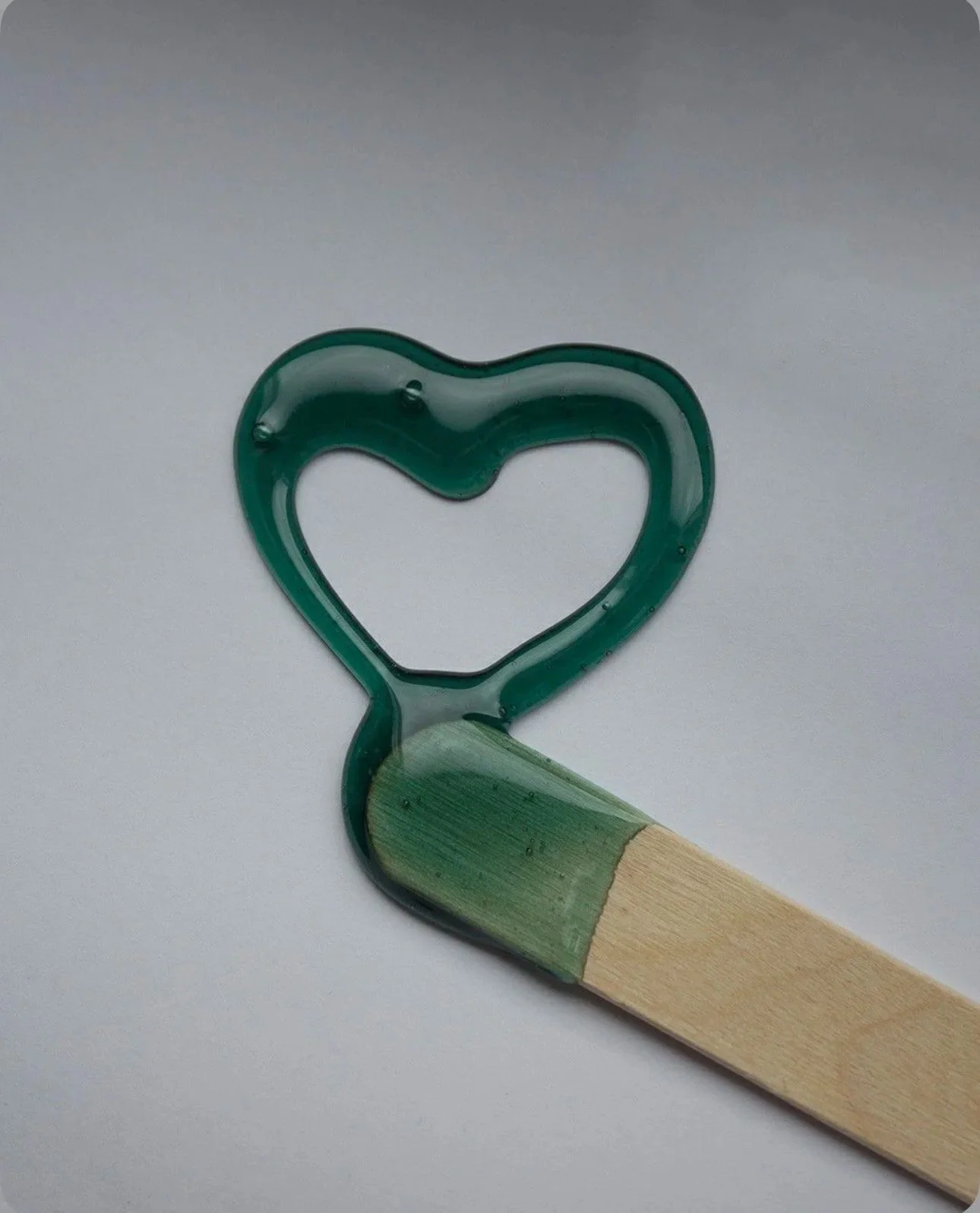 A heart-shaped paint in green, featuring a wooden stick, perfect for artistic endeavors.