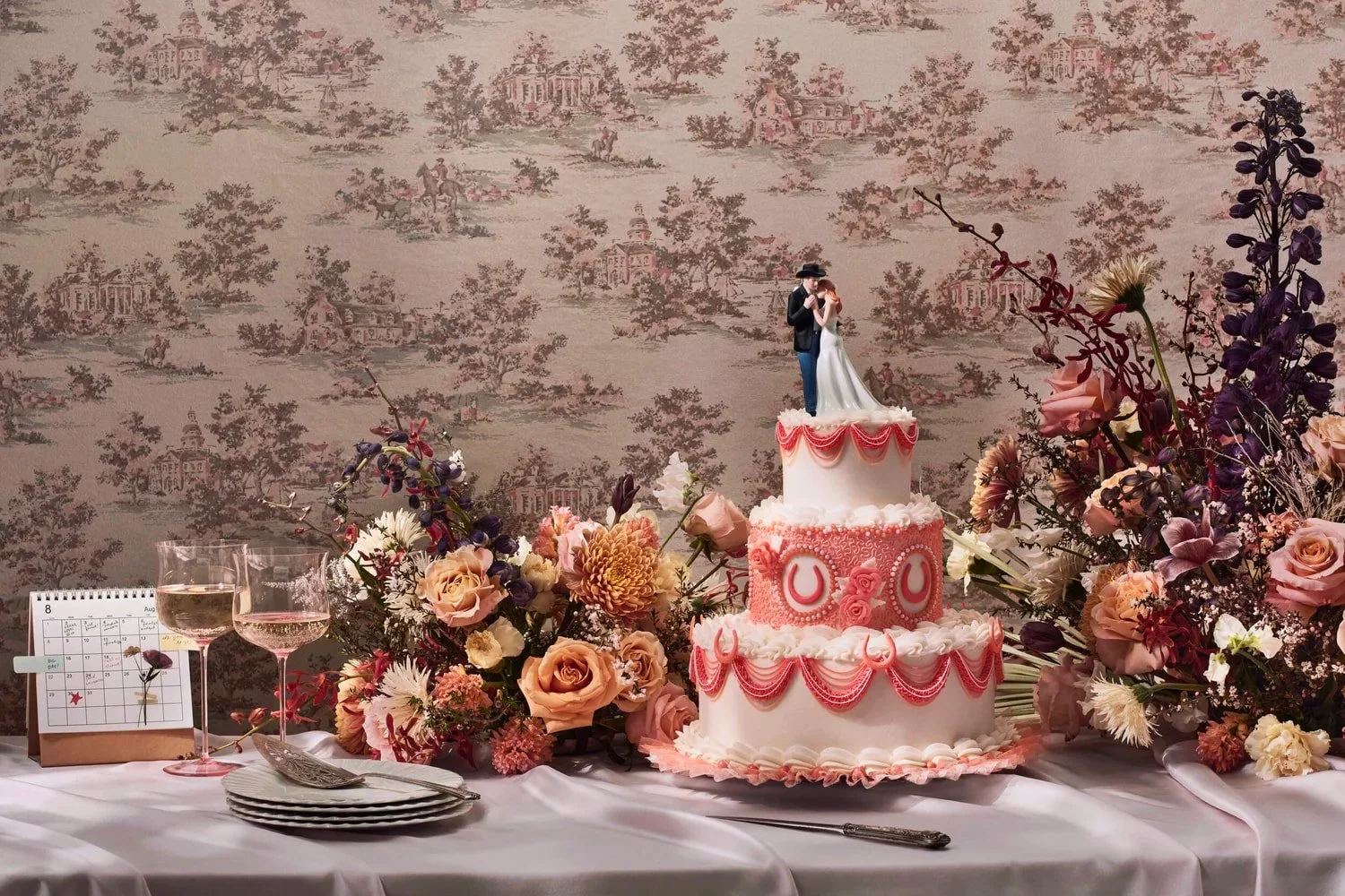 A three-tiered wedding cake adorned with white frosting and floral decorations, featuring a couple figurine on top.
