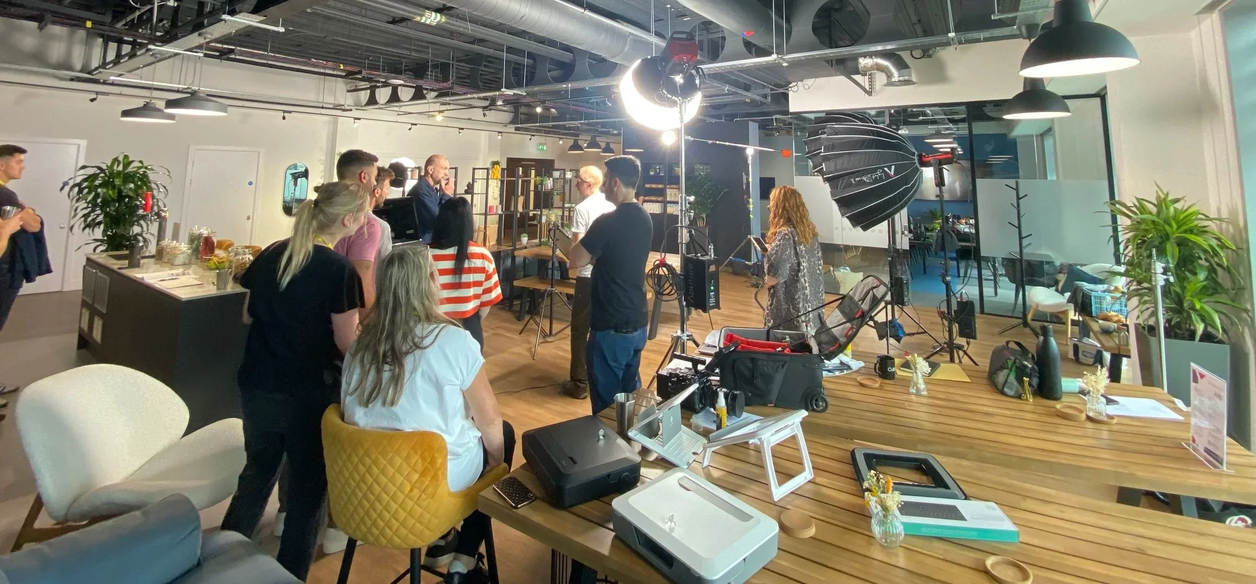 People gathered in a modern indoor space with professional filming equipment, cameras, and lighting, as they prepare for a video shoot or interview.