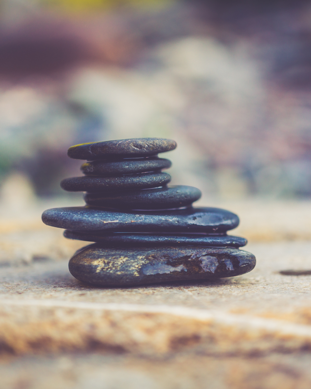 Stacked black stones on a sandy surface with blurred background.