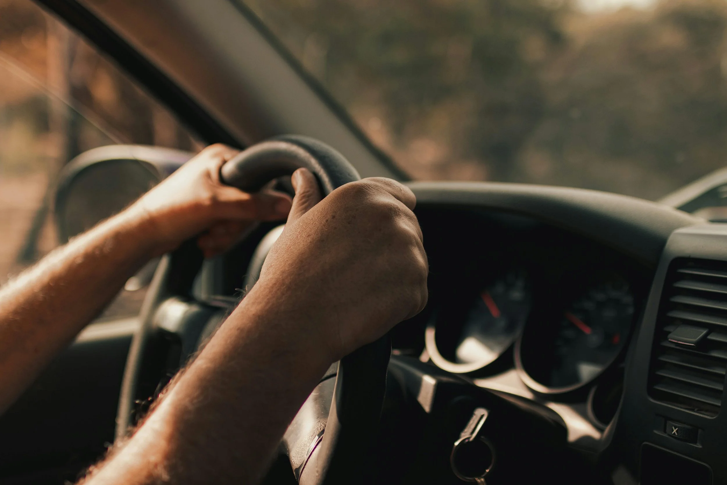 Mains d'une personne au volant d'une voiture, vues de l'intérieur, conduite en route en milieu rural.
