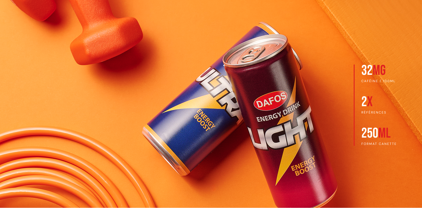 Deux canettes d'énergie DAFOS Boost, une bleue et une rouge, l'une à côté de l'autre, sur une surface orange, avec des haltères orange en haut à gauche et un tapis orange en haut à droite.