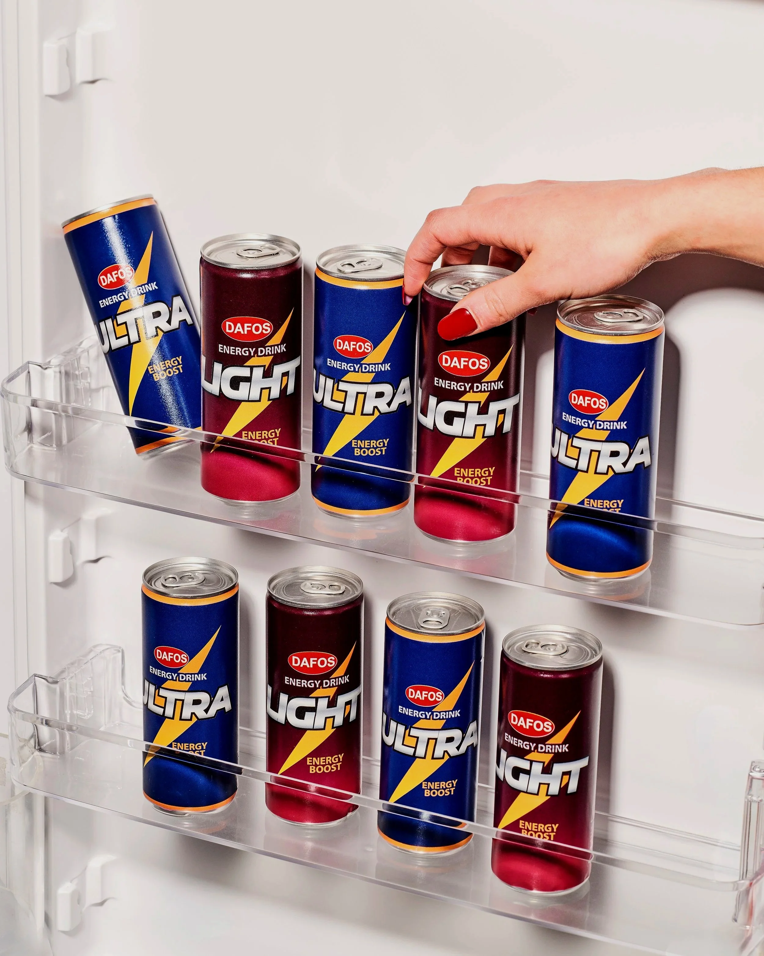 Une main avec des ongles rouges saisit une canette rouge dans un réfrigérateur contenant plusieurs canettes de boisson énergisante DAFOS ULTRA ENERGY BOOST.