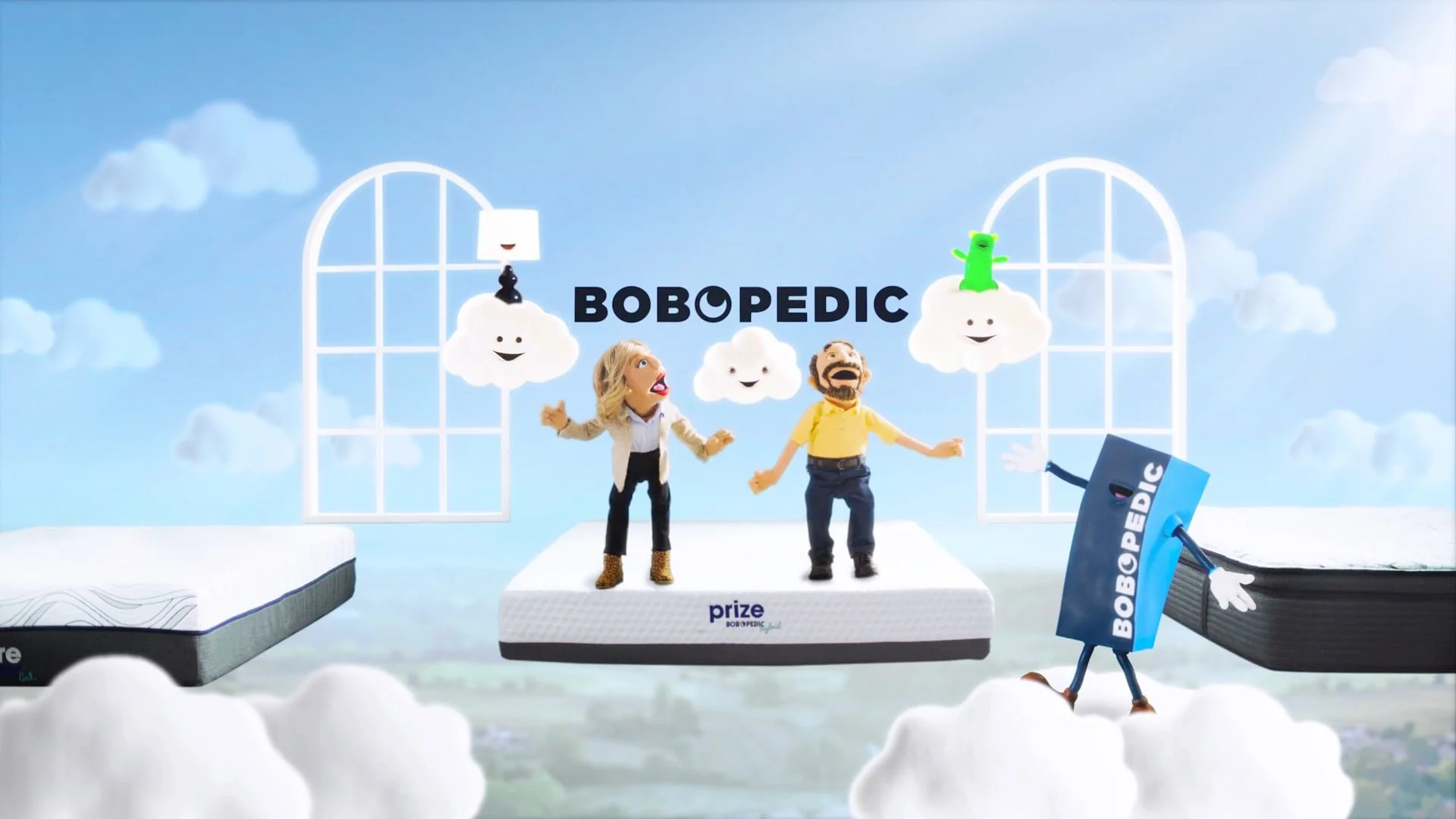 A colorful animated scene with two puppet characters, a woman and a man, standing on a cloud-like platform with the word 'BOBOPEDIC' in the background. The scene features whimsical clouds, windows, and a playful environment.