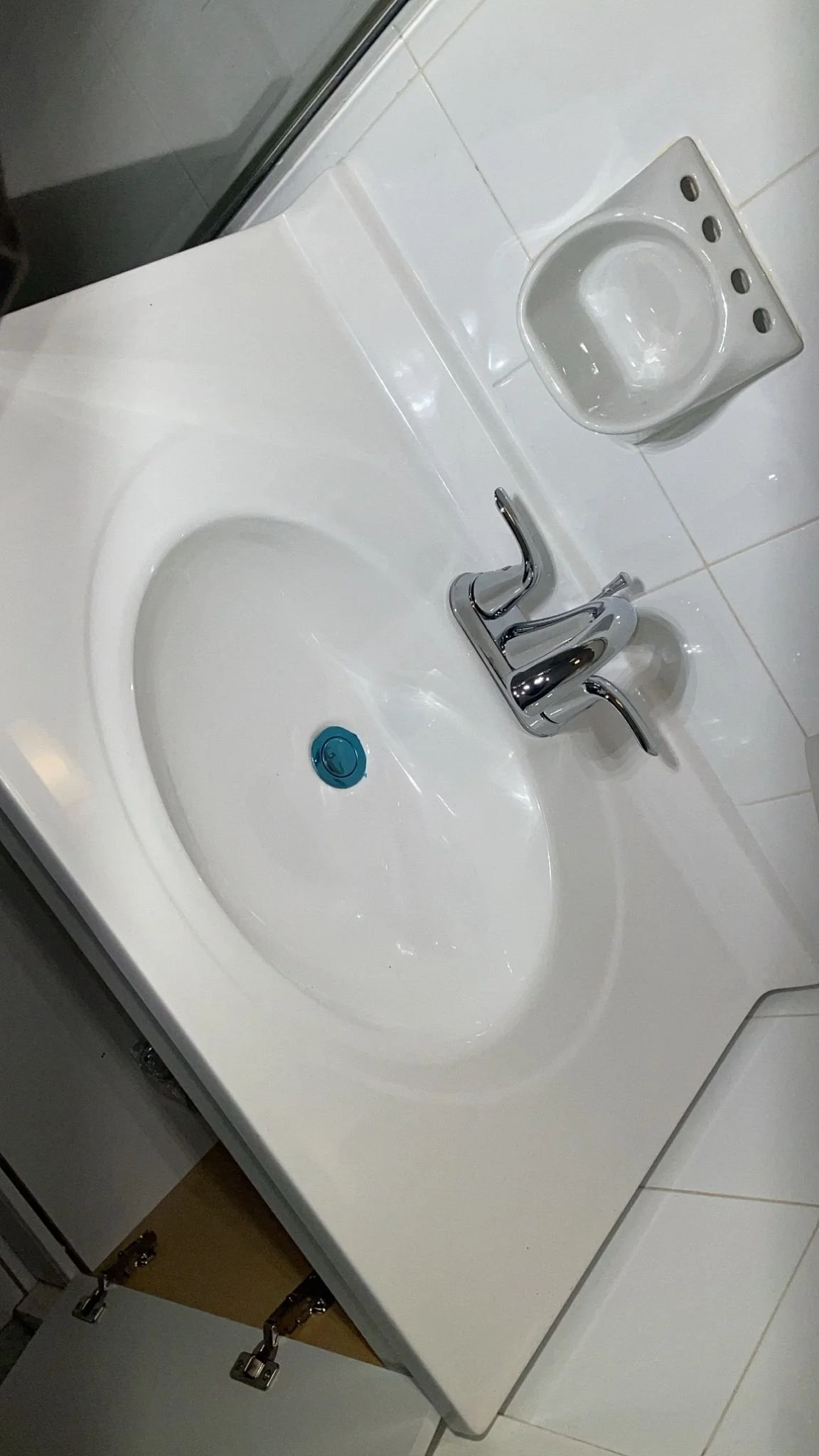 A bathroom sink with a chrome faucet, a white soap dish holder, and a blue drain stopper.