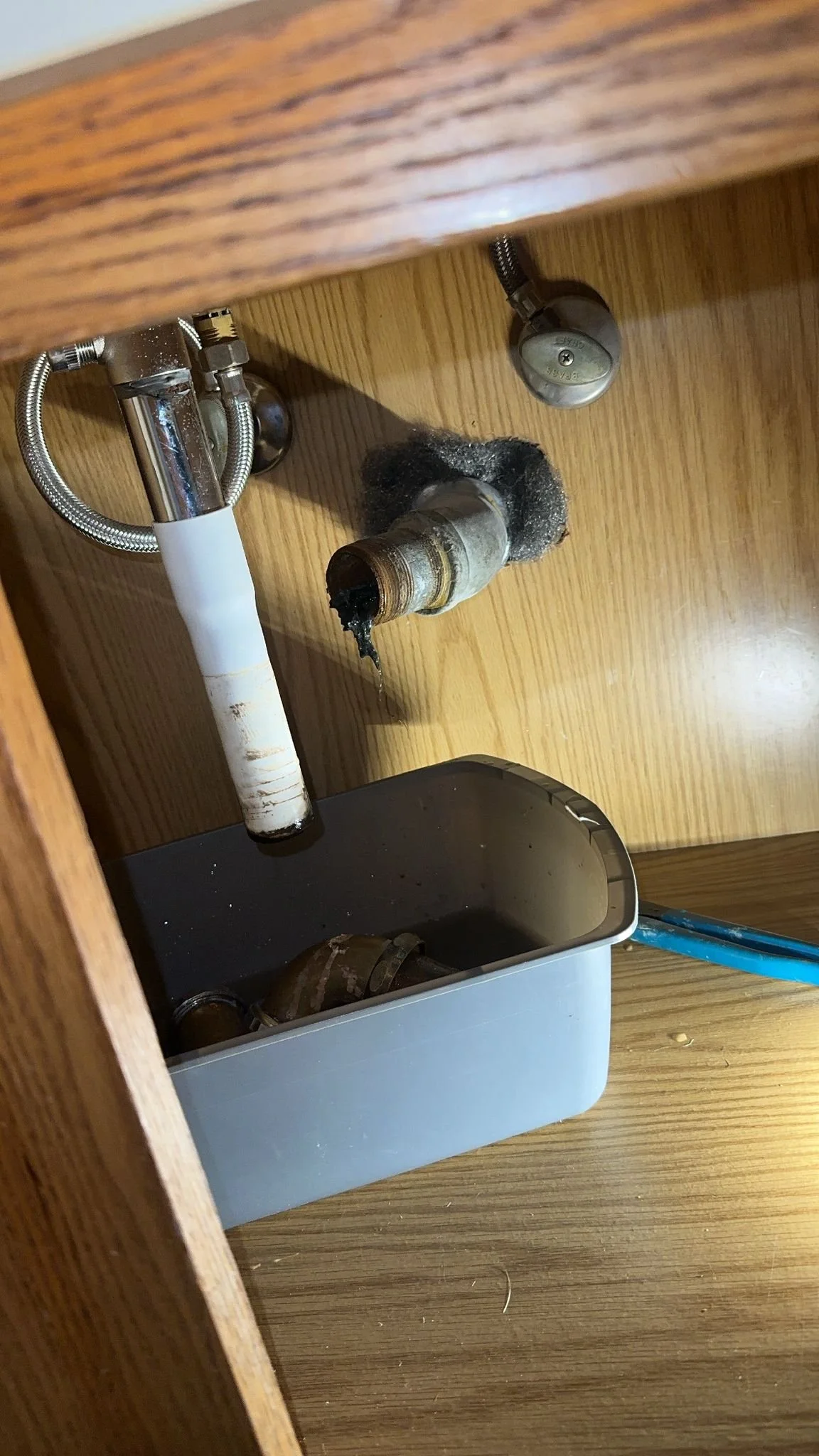 Underneath a kitchen sink showing a disconnected pipe, a plumbing trap, and a container catching residual water.