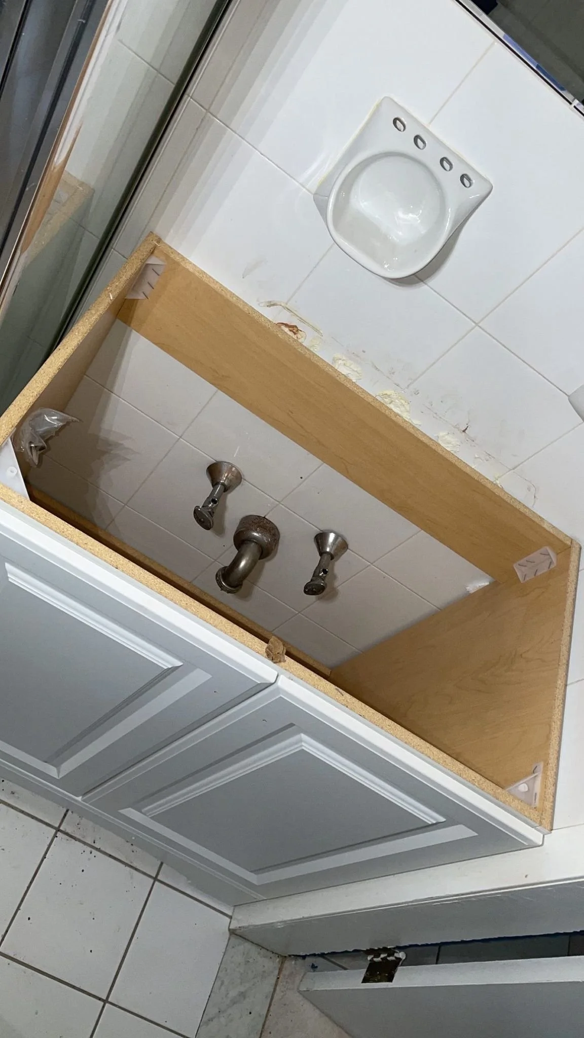 Bathroom vanity being installed with plumbing fixtures visible, and a wall-mounted sink installed on a tiled wall.