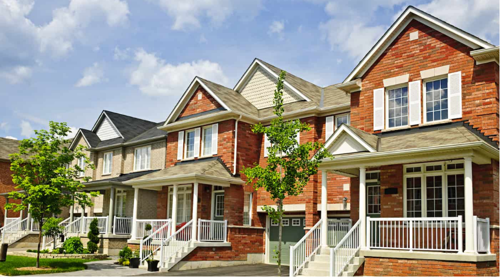 A row of brick townhomes with single garage underneath, small porches, and a cheery blue sky with clouds.