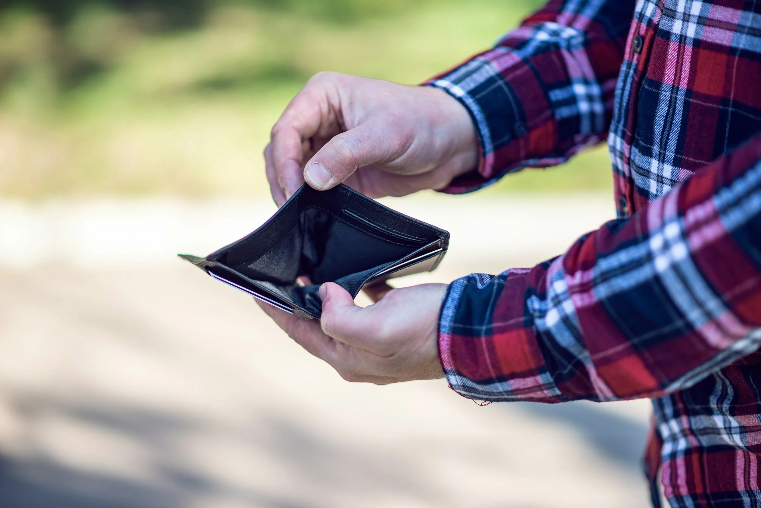 A man in a red plaid flannel holds open an empty, black leather wallet.