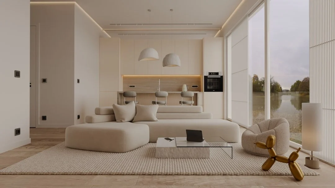 Modern living room with oversized beige sofa, armchair, balloon dog sculpture, and large window with outdoor view