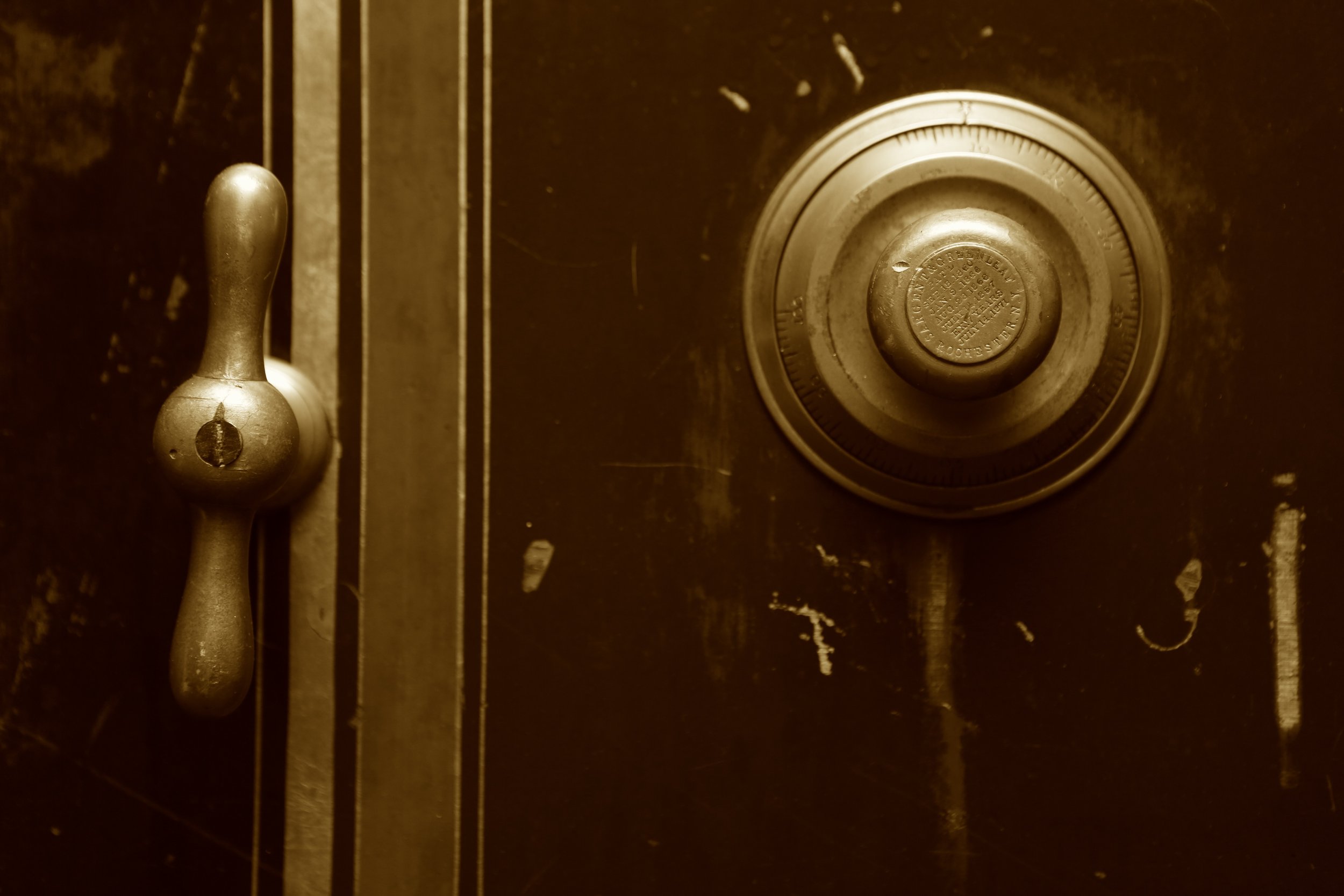 Close-up image of a round combination safe dial and a handle on a dark, worn surface.