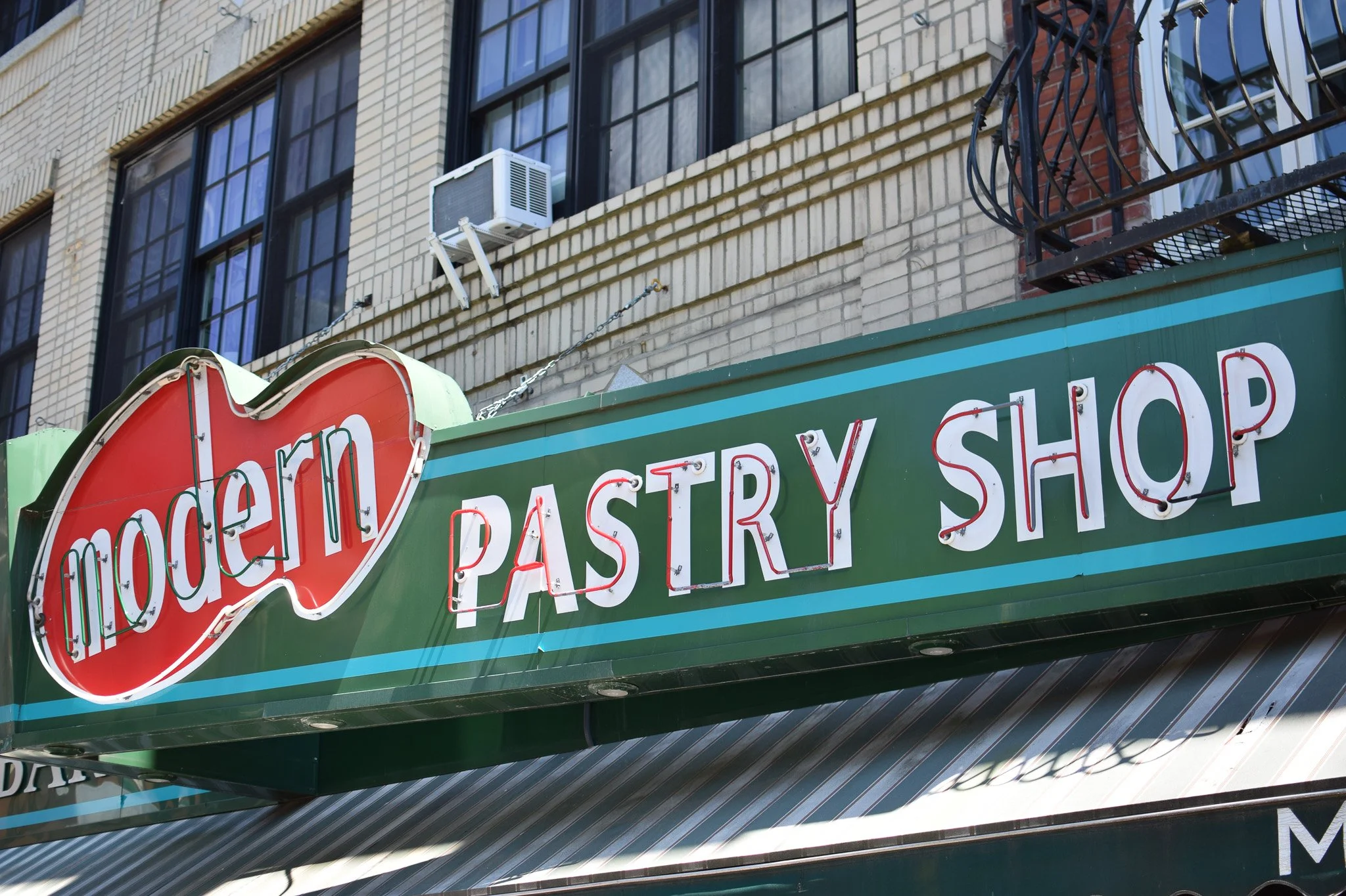 Close-up of a green restaurant sign with red and white neon lights, partially visible, with a brick building and windows in the background.