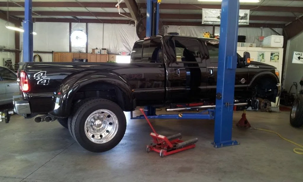 A black pickup truck elevated on a blue hydraulic lift inside a garage or workshop, missing its wheels.