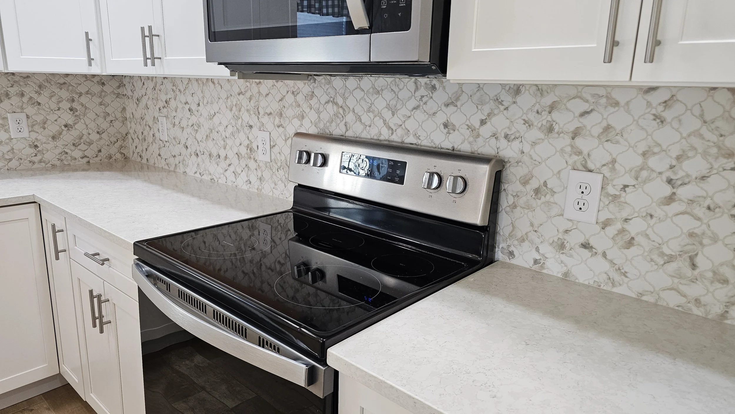 Kitchen with white cabinets, marble backsplash, and stainless steel stove and microwave.